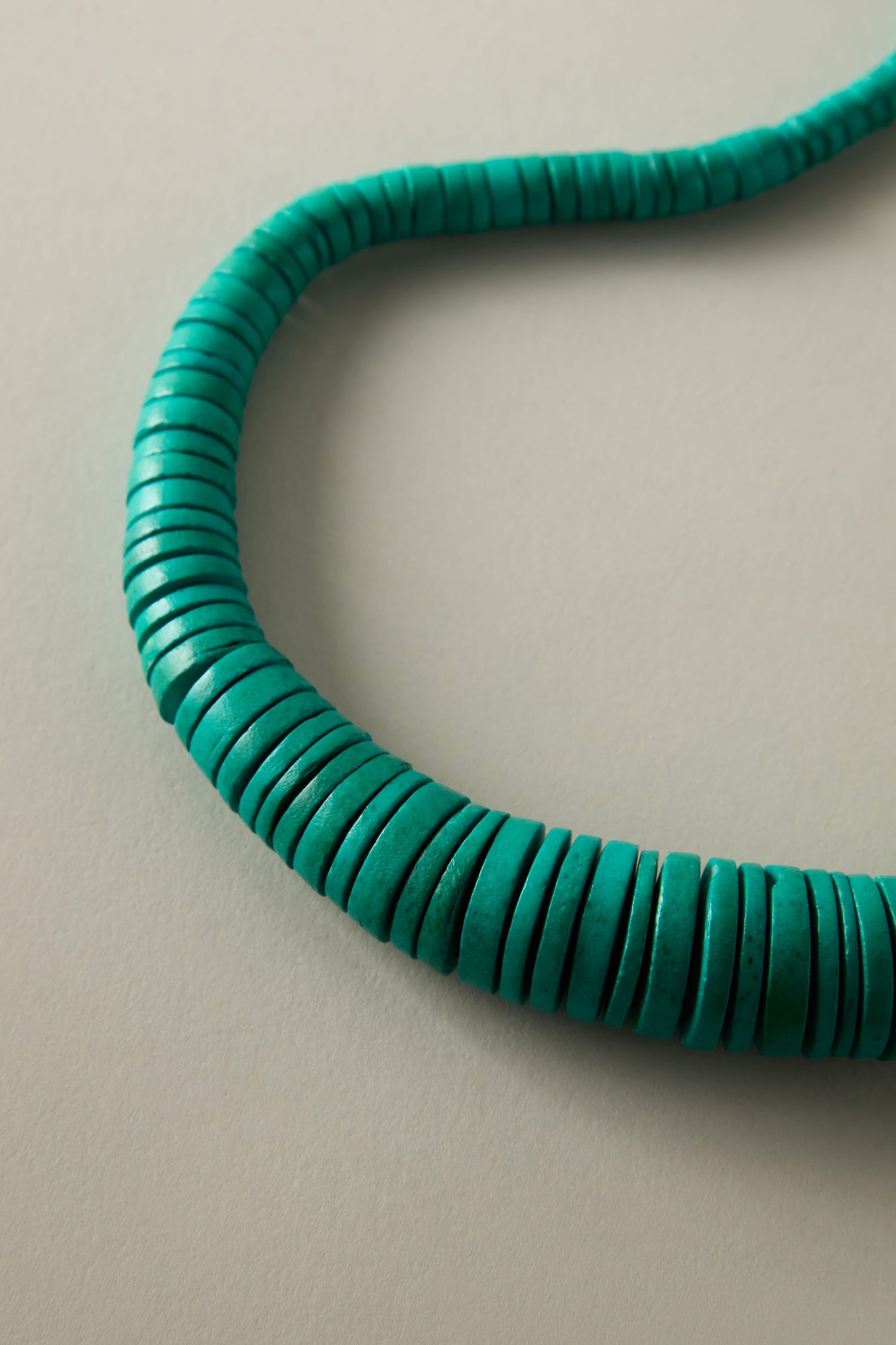 Set against a plain beige backdrop, the Graduated Coco Disc Necklace features round, green turquoise beads, exemplifying Philippine craftsmanship and a dedication to ethically sourced materials.