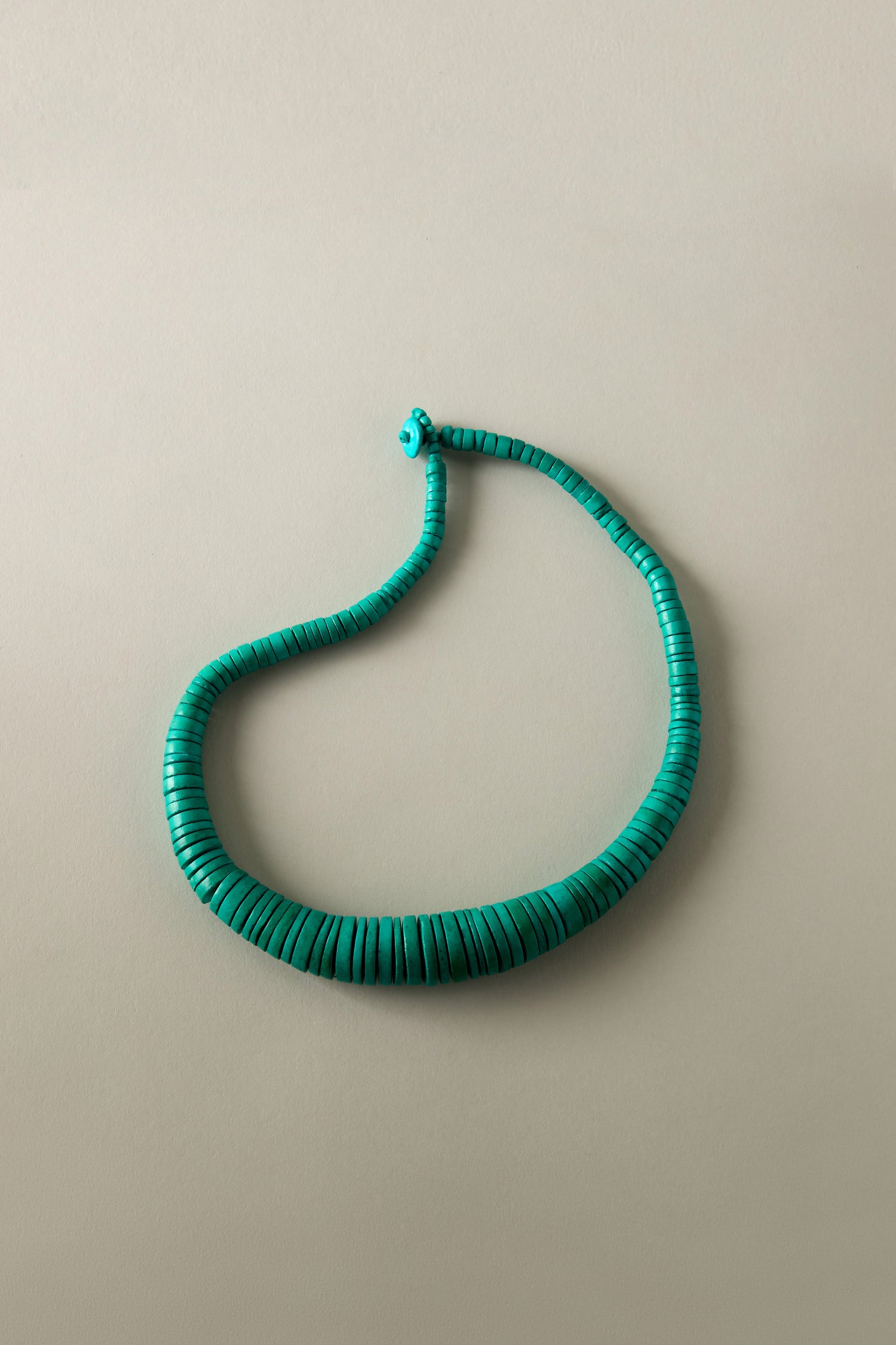 The Graduated Coco Disc Necklace, featuring flat round turquoise-colored beads, is elegantly displayed on a neutral background, highlighting the exquisite craftsmanship of the Philippines.