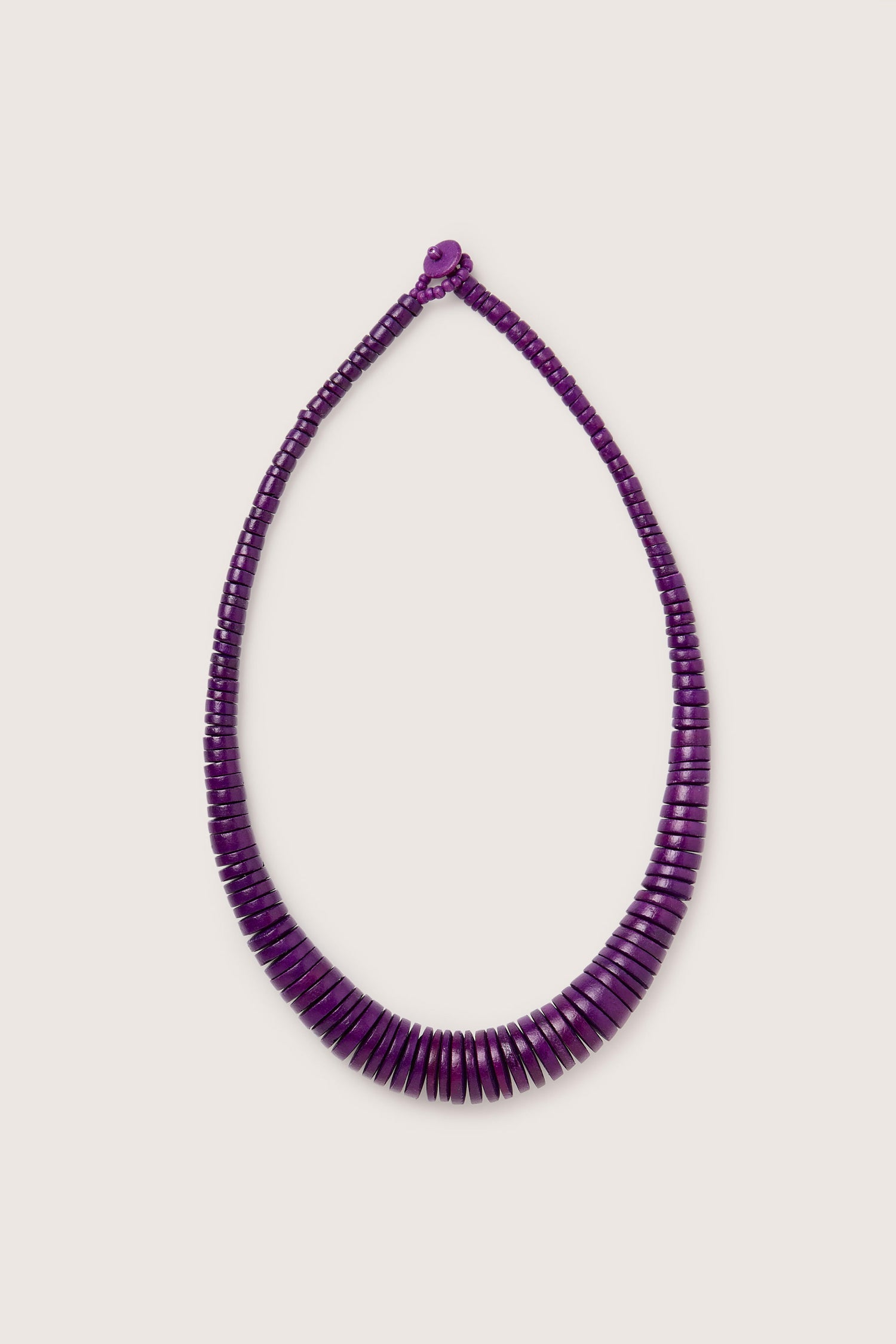 The Short Graduated Coco Disc Necklace by Lotusfeet is a handmade piece featuring disc-shaped beads, adorned with purple accents and arranged in a captivating size pattern.