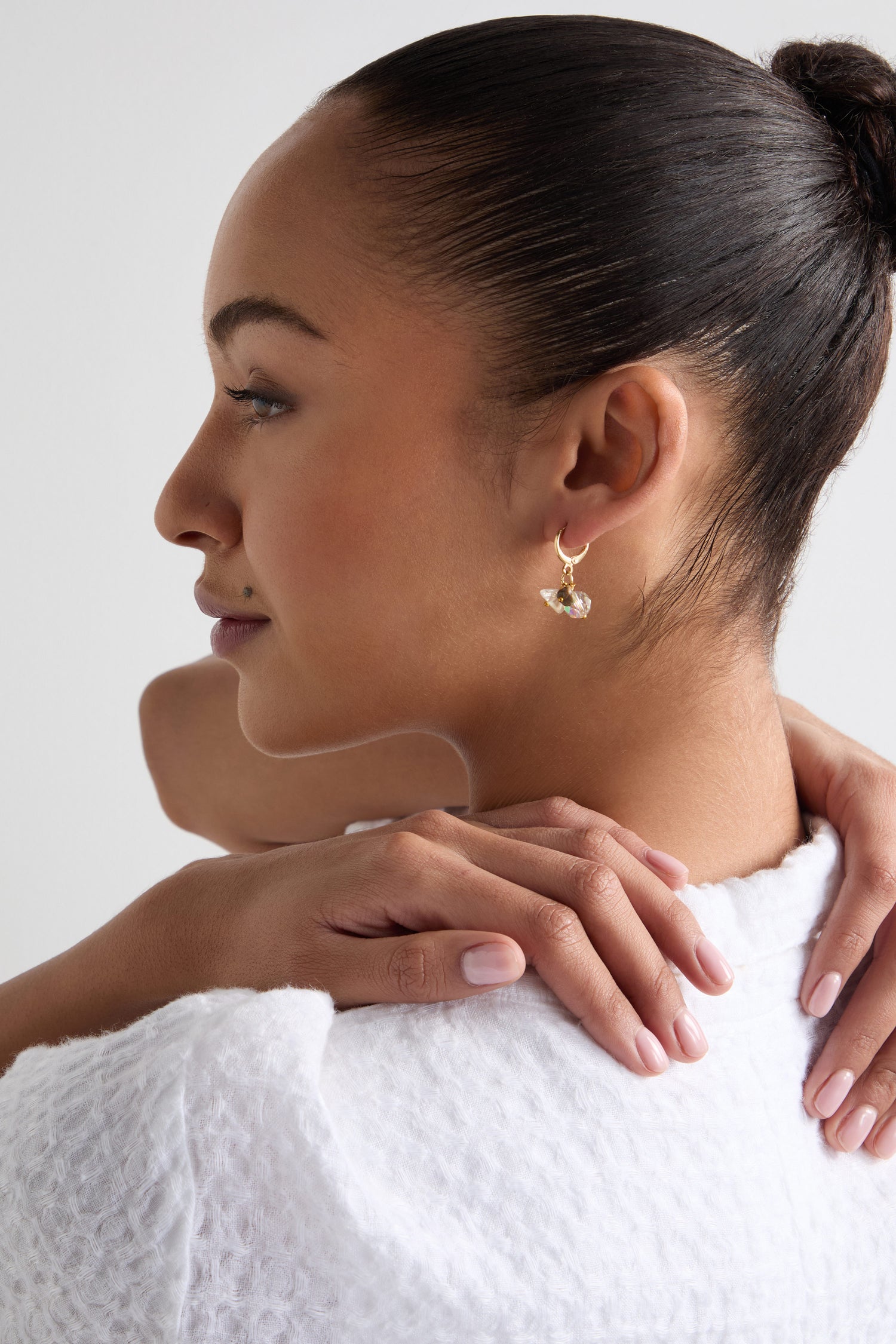 With hair tied back, a person wearing Citrine and Rhyolite Bead Earrings and a white textured top rests their hands on their shoulder.