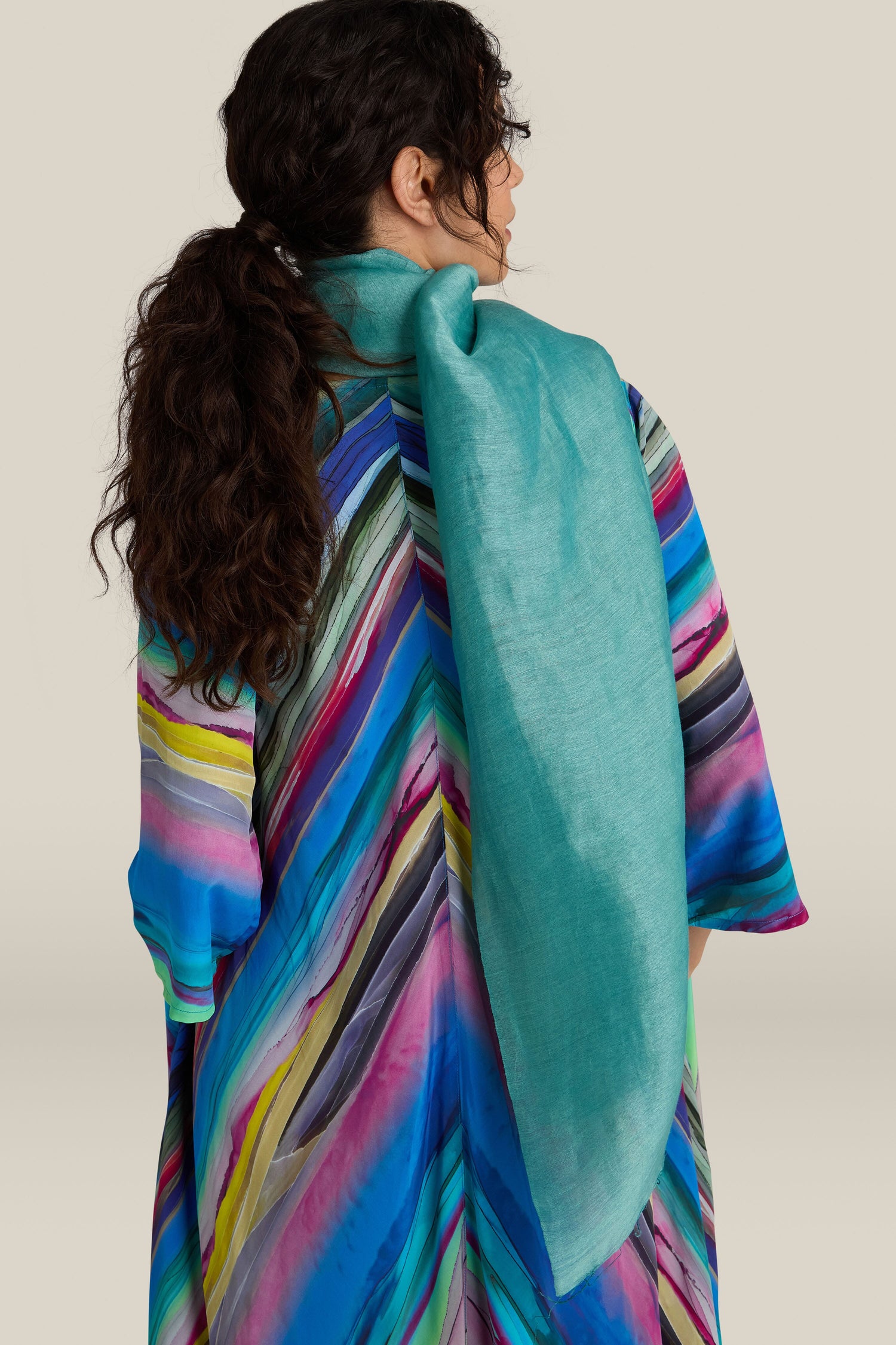 A person with long, wavy hair in a ponytail is wearing a colorful, striped garment and the Soft Linen Scarf, facing away from the camera.