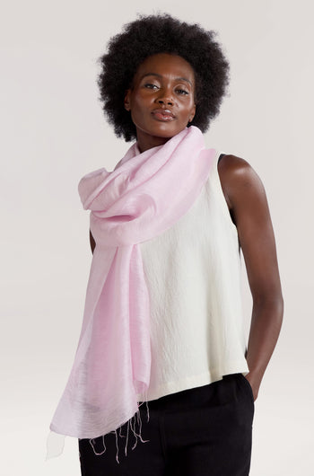 A person with dark curly hair is wearing a sleeveless white top and a Soft Linen Scarf in pink, standing against a plain background.