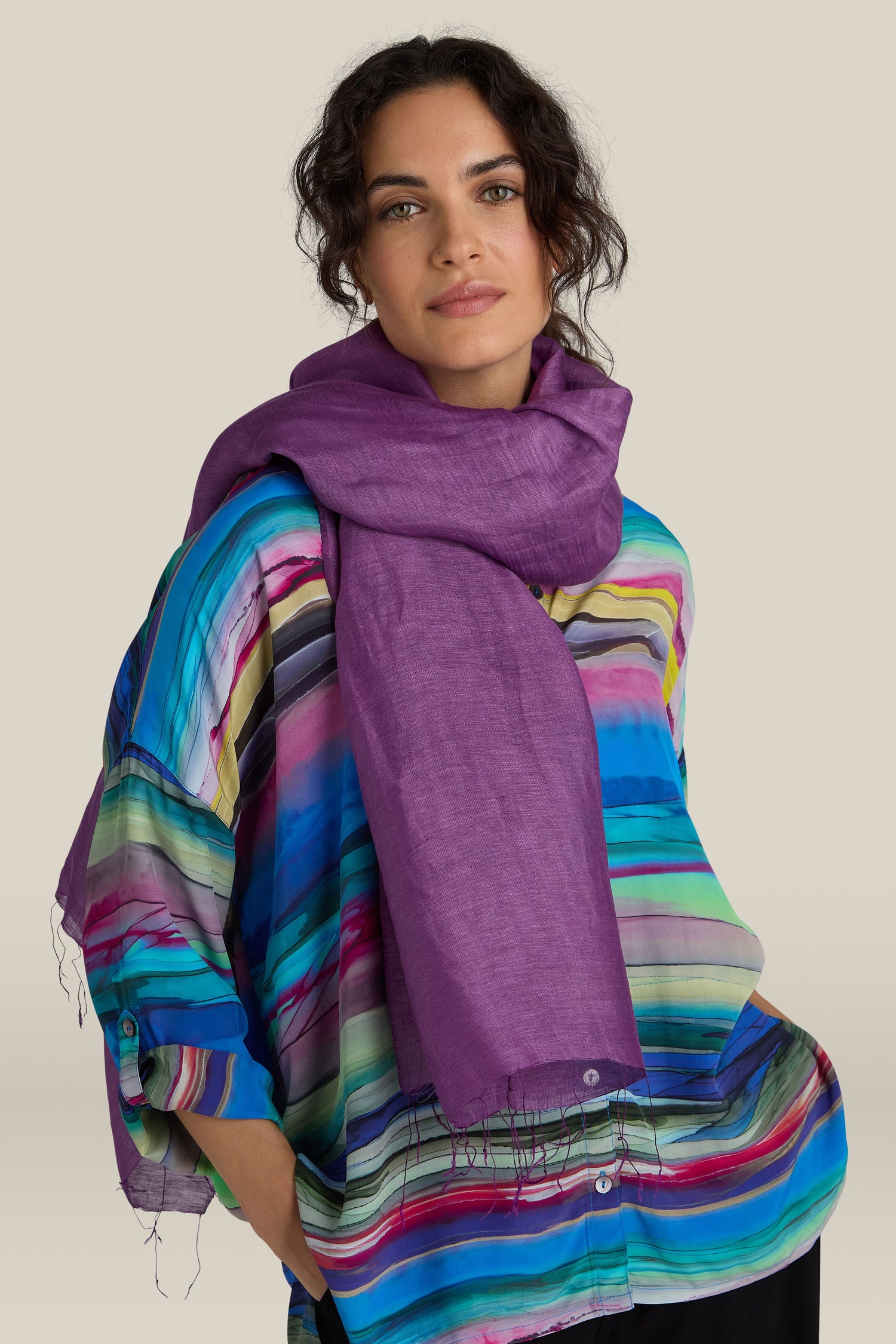 A person wearing a colorful striped shirt and a luxurious Soft Linen Scarf in purple looks at the camera against a beige background.