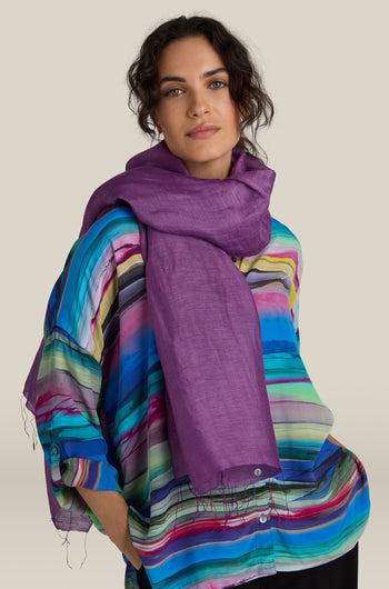 A person wearing a colorful striped shirt and a luxurious Soft Linen Scarf in purple looks at the camera against a beige background.