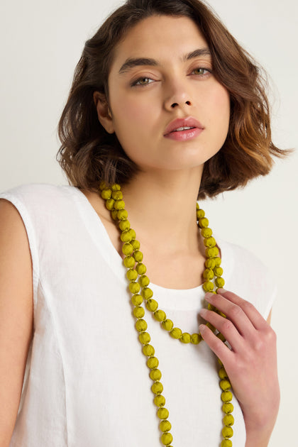 A woman with short brown hair and a white sleeveless top wears the Handmade Long Silk Spheres Necklace in yellow, looking at the camera with a neutral expression.