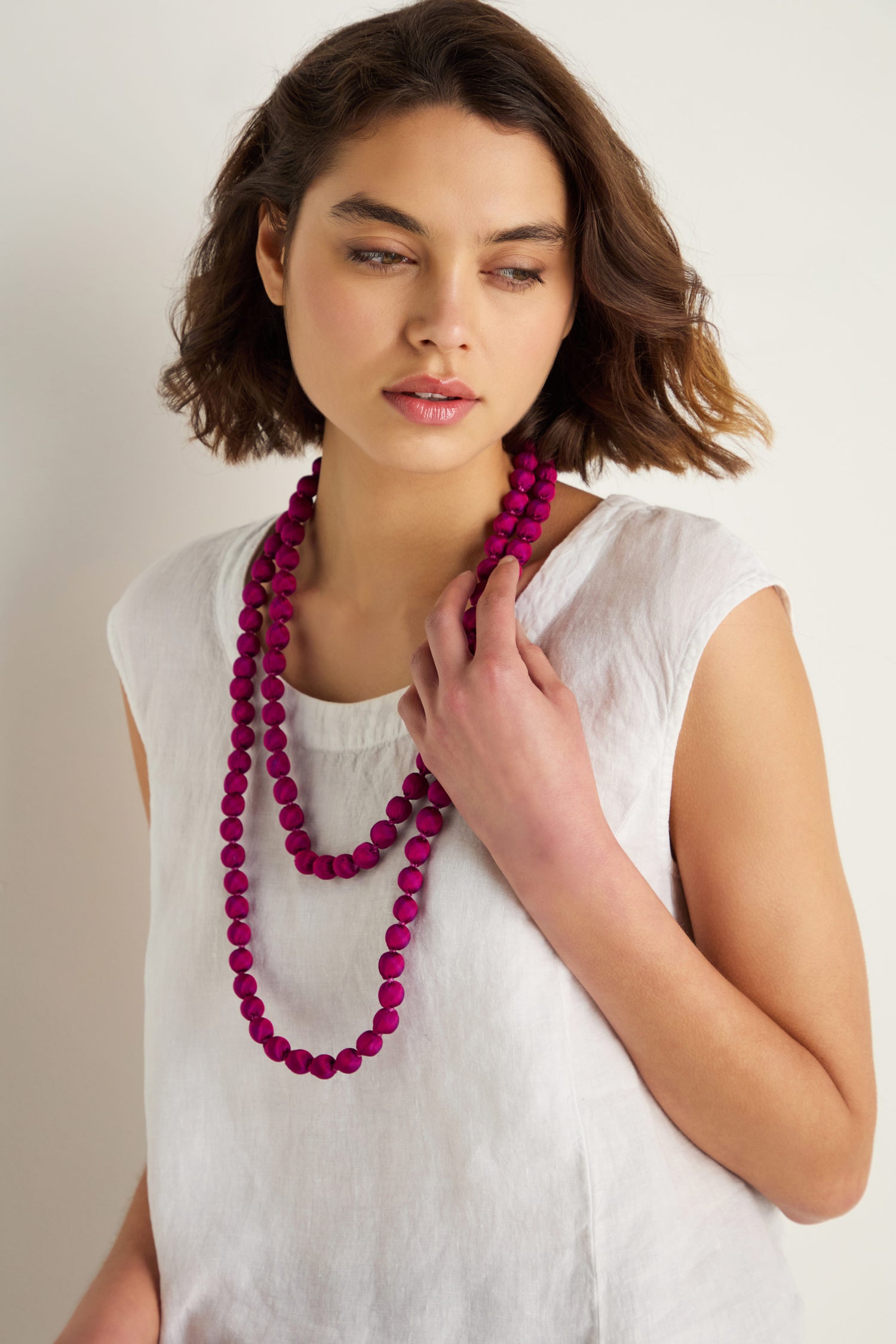 A woman in a white sleeveless top wears two Handmade Long Silk Spheres Fuchsia Necklaces, layered against a plain light background.