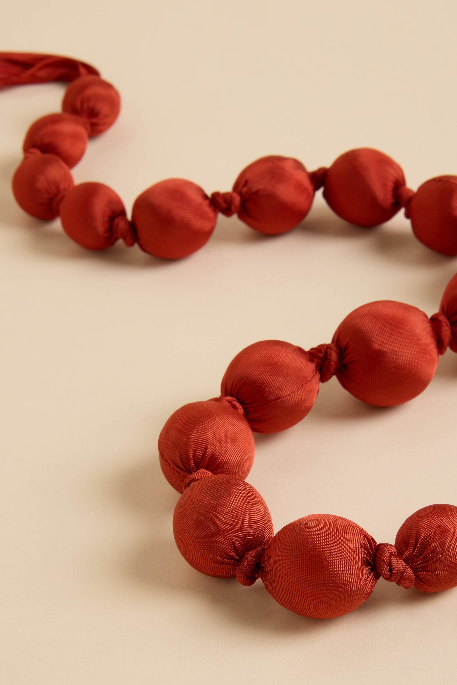 Two strands of round red beads create the elegant Handmade Silk Spheres Necklace, beautifully displayed on a light beige surface.
