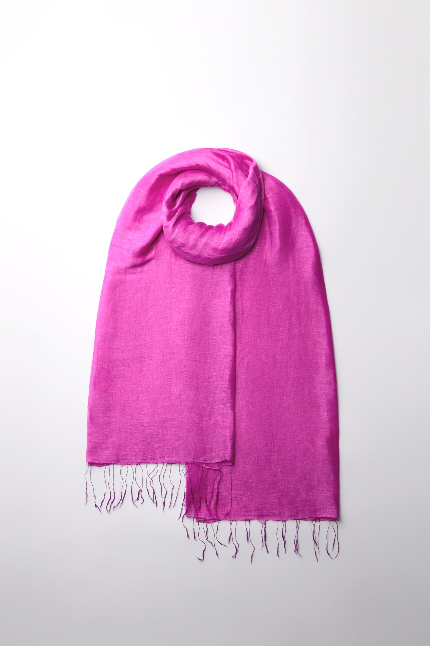 Bohemian accessory alert: the Soft Linen Fringe Scarf in pink, artfully looped on a light gray background. This versatile piece blends elegance and charm effortlessly.