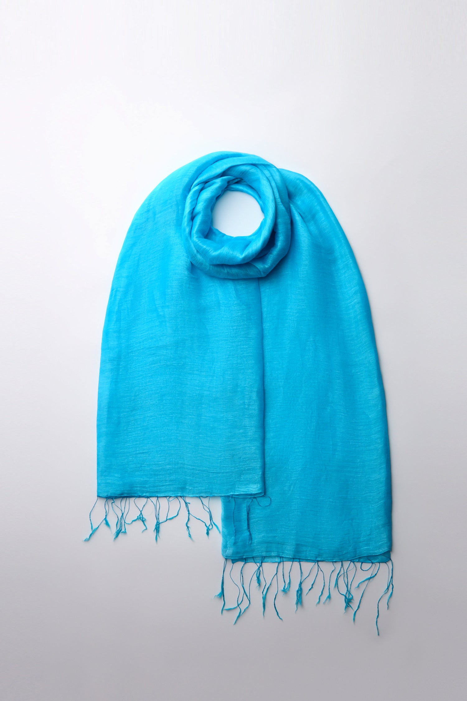 The Soft Linen Fringe Scarf in bright blue is showcased on a plain white background, highlighting its soft linen fabric and fringed edges, making it an essential versatile wardrobe piece.