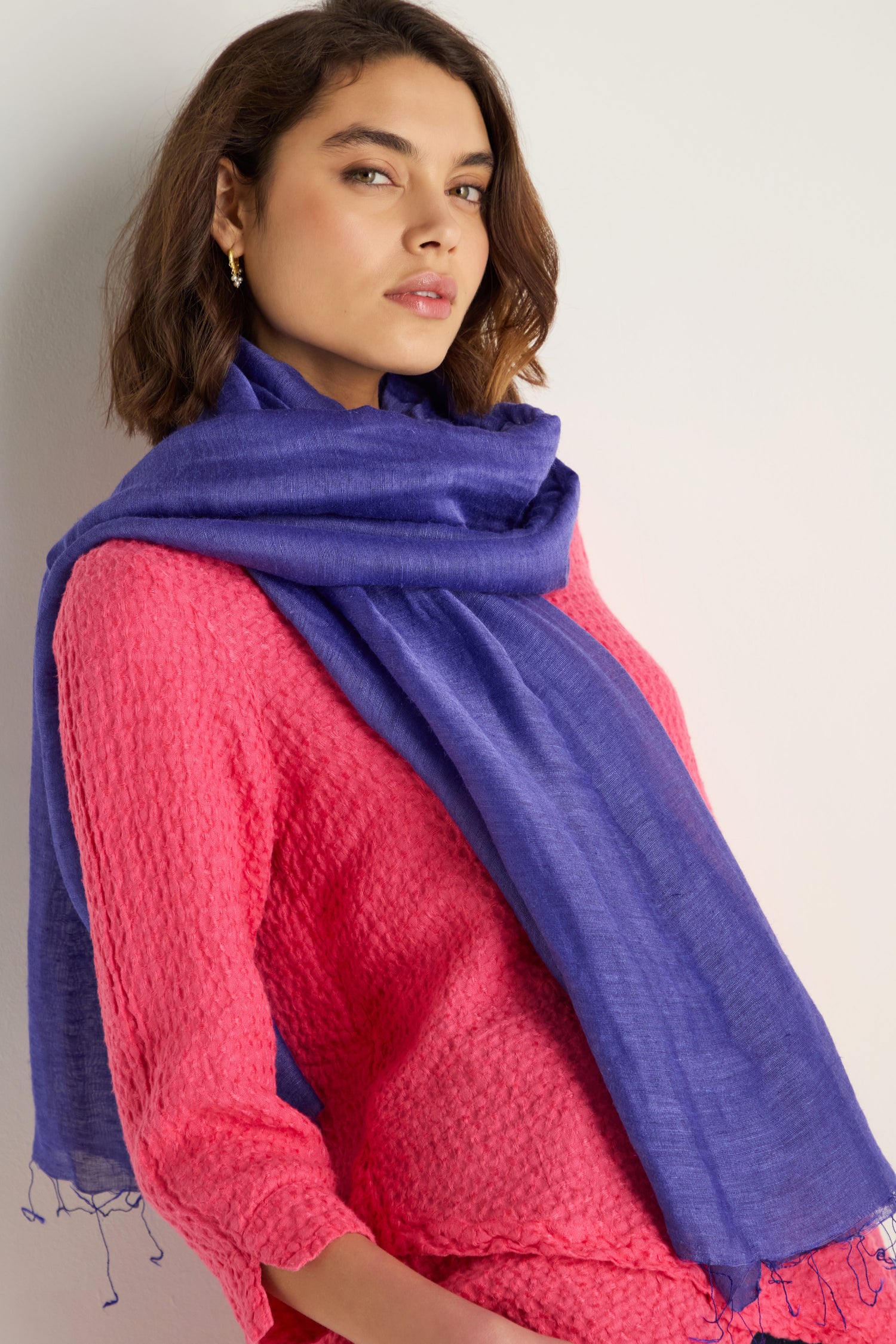 A woman stands against a neutral background wearing a textured pink top and the Soft Linen Fringe Scarf in blue.