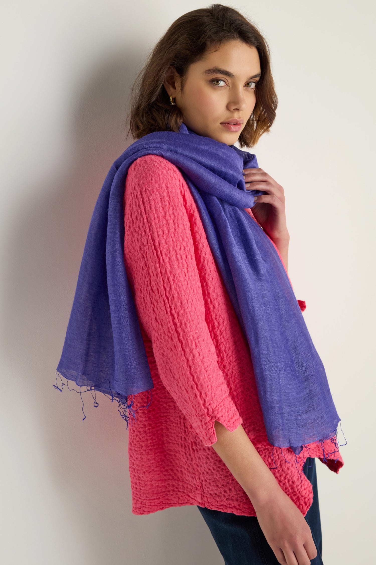 A woman in a textured pink top wears the Soft Linen Fringe Scarf against a plain light background, her neutral expression highlighting this scarf’s lightweight layering appeal.