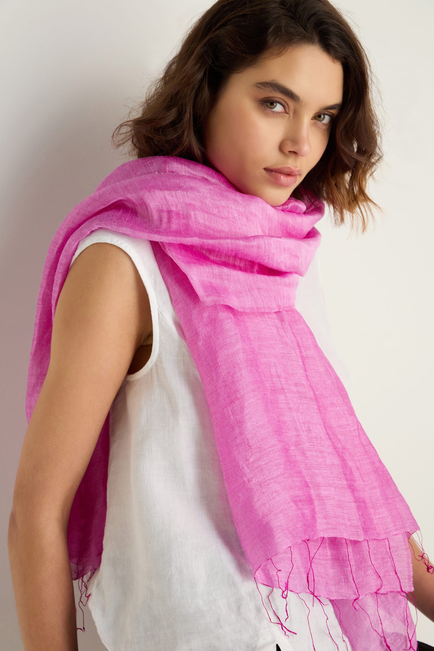 A woman wears a white sleeveless top and a Soft Linen Fringe Scarf in bright pink, draped around her shoulders, standing against a plain white background.