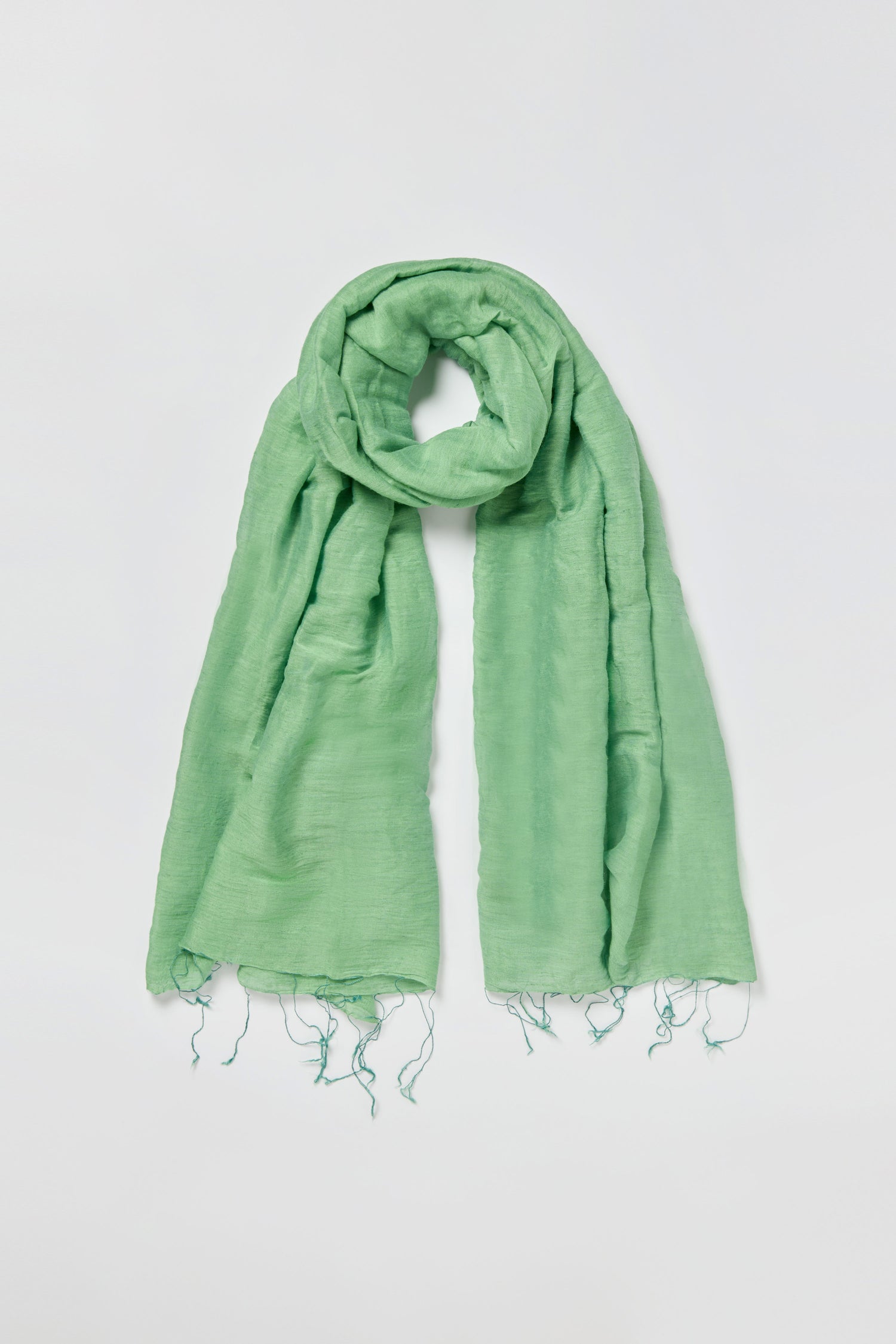 The Olive Soft Linen Fringe Scarf is a lightweight, light green accessory with a slightly crinkled texture and fringed ends, crafted from a soft linen-silk blend and shown laid flat on a white background.