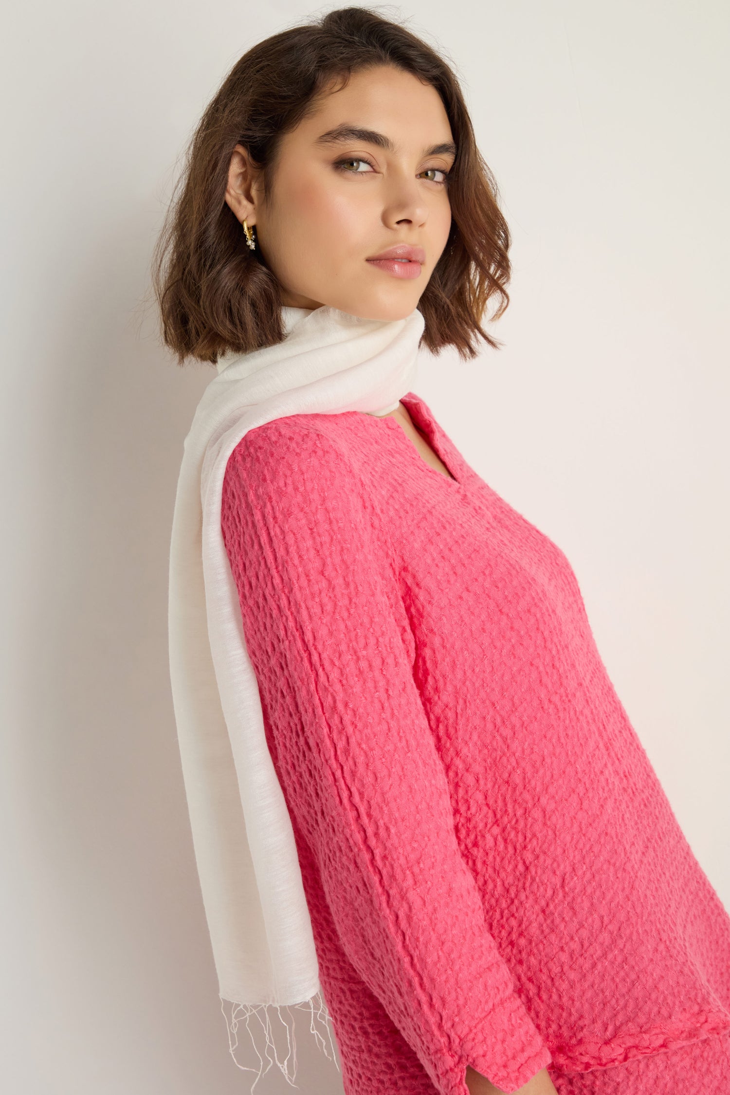 A woman with short brown hair wears a textured pink top and a Soft Linen Fringe Scarf draped around her neck, standing against a plain light background.