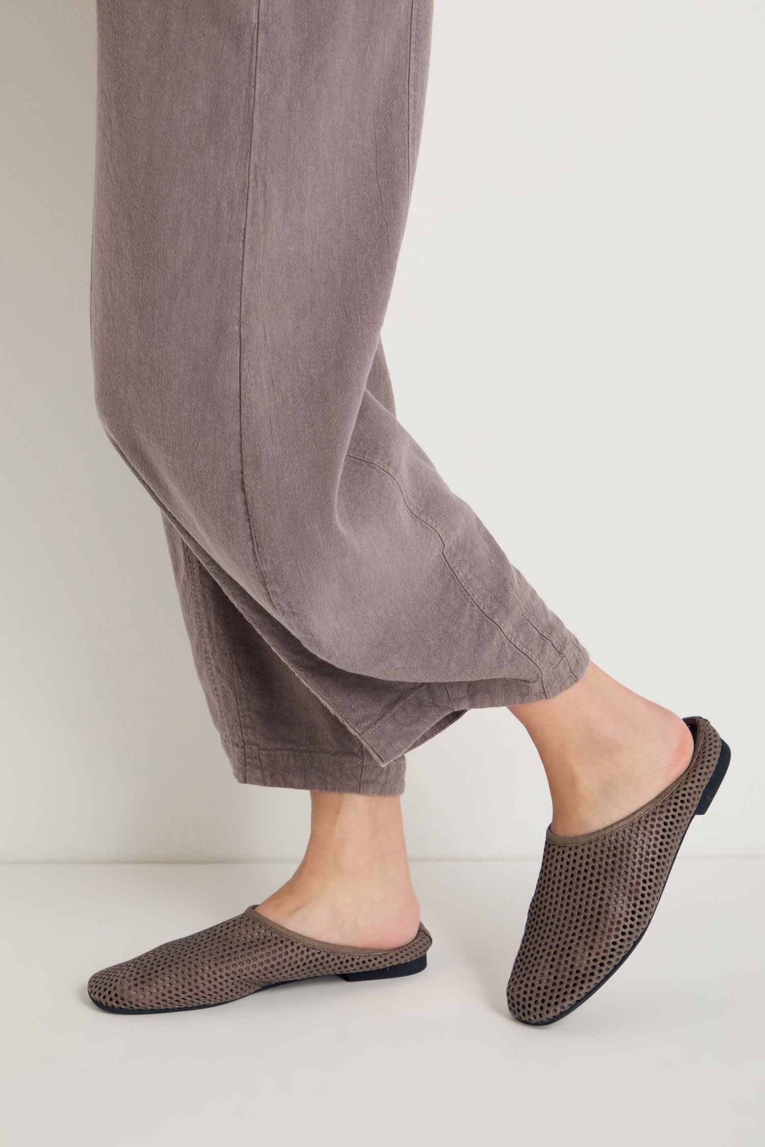 A person wearing loose mauve pants and Mesh Leather Slip on Shoes, brown and handmade in Europe, stands against a plain light background.