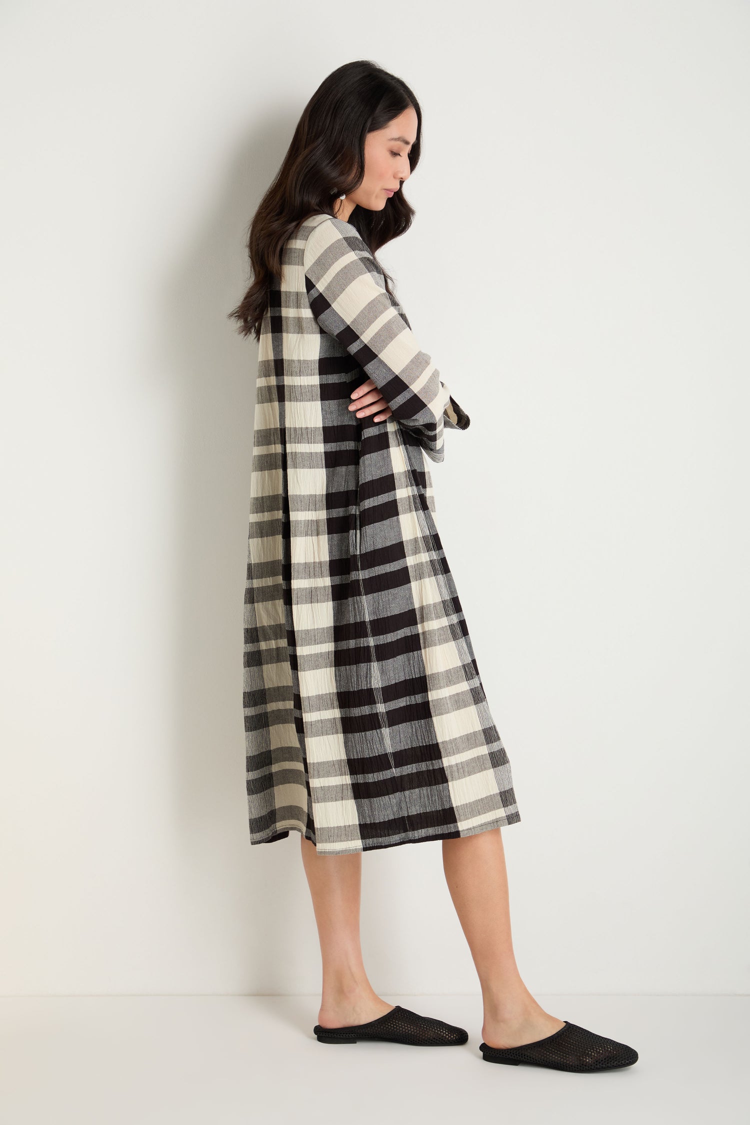 Woman in a long-sleeve, black and white plaid dress stands sideways against a white wall, wearing Mesh Leather Slip on Shoes—breathable, handmade in Europe.