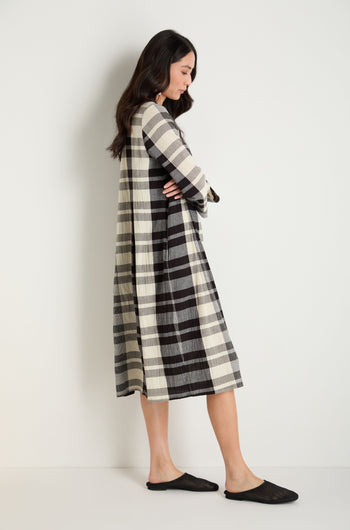 Woman in a long-sleeve, black and white plaid dress stands sideways against a white wall, wearing Mesh Leather Slip on Shoes—breathable, handmade in Europe.
