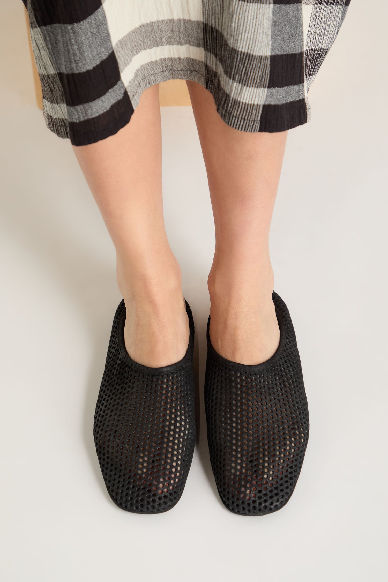 Model wears Mesh Leather Slip on Shoes, featuring breathable mesh leather and handmade in Europe, paired with a black-and-white plaid skirt on a light surface.