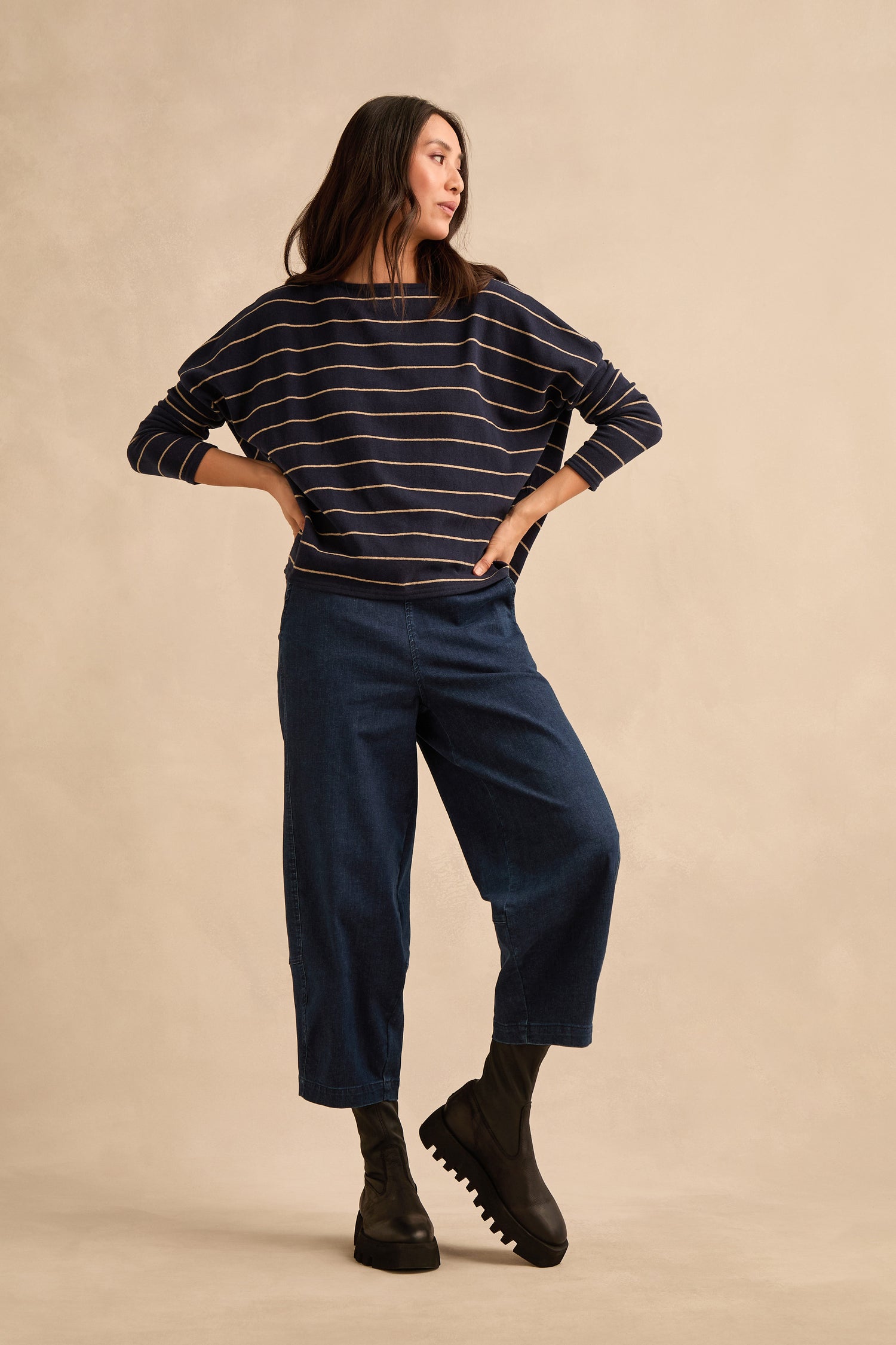 Woman stands in a relaxed pose wearing a navy striped sweater, wide-leg blue jeans, and Platform Napa Leather Stretch Boots with black cleated soles against a beige background.
