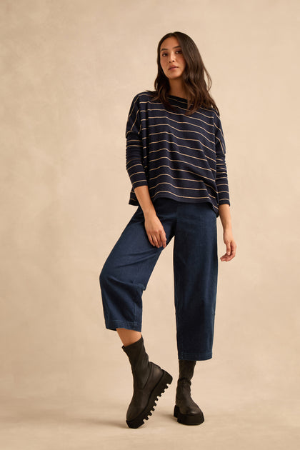 A woman stands against a beige studio backdrop wearing a navy striped long-sleeve top, wide-leg cropped denim pants, and Platform Napa Leather Stretch Boots with a cleated platform sole.