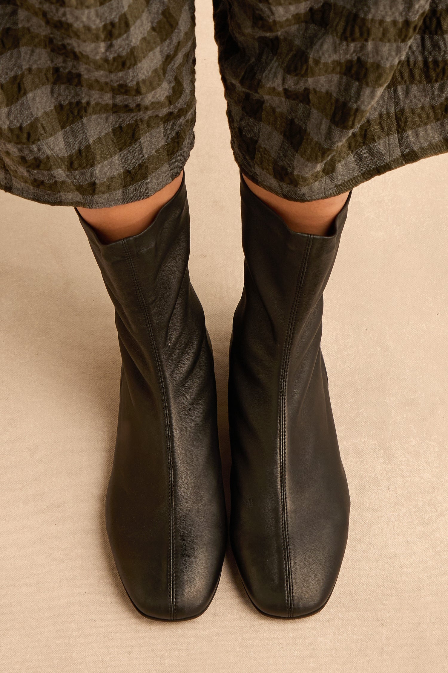 Person wearing Slim Napa Leather Stretch Boots and plaid pants, standing on a beige surface.