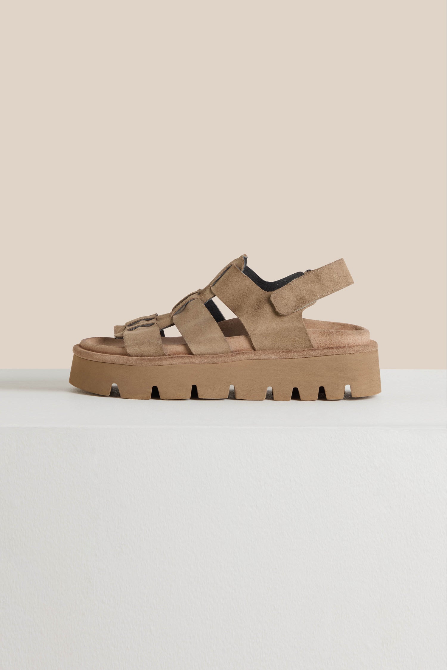 Suede Platform Velcro Sandals with brown chunky soles rest elegantly on a light surface against a beige backdrop. Featuring adjustable Velcro straps, these fashionable sandals offer style and comfort, expertly crafted in Italy for a luxurious touch.