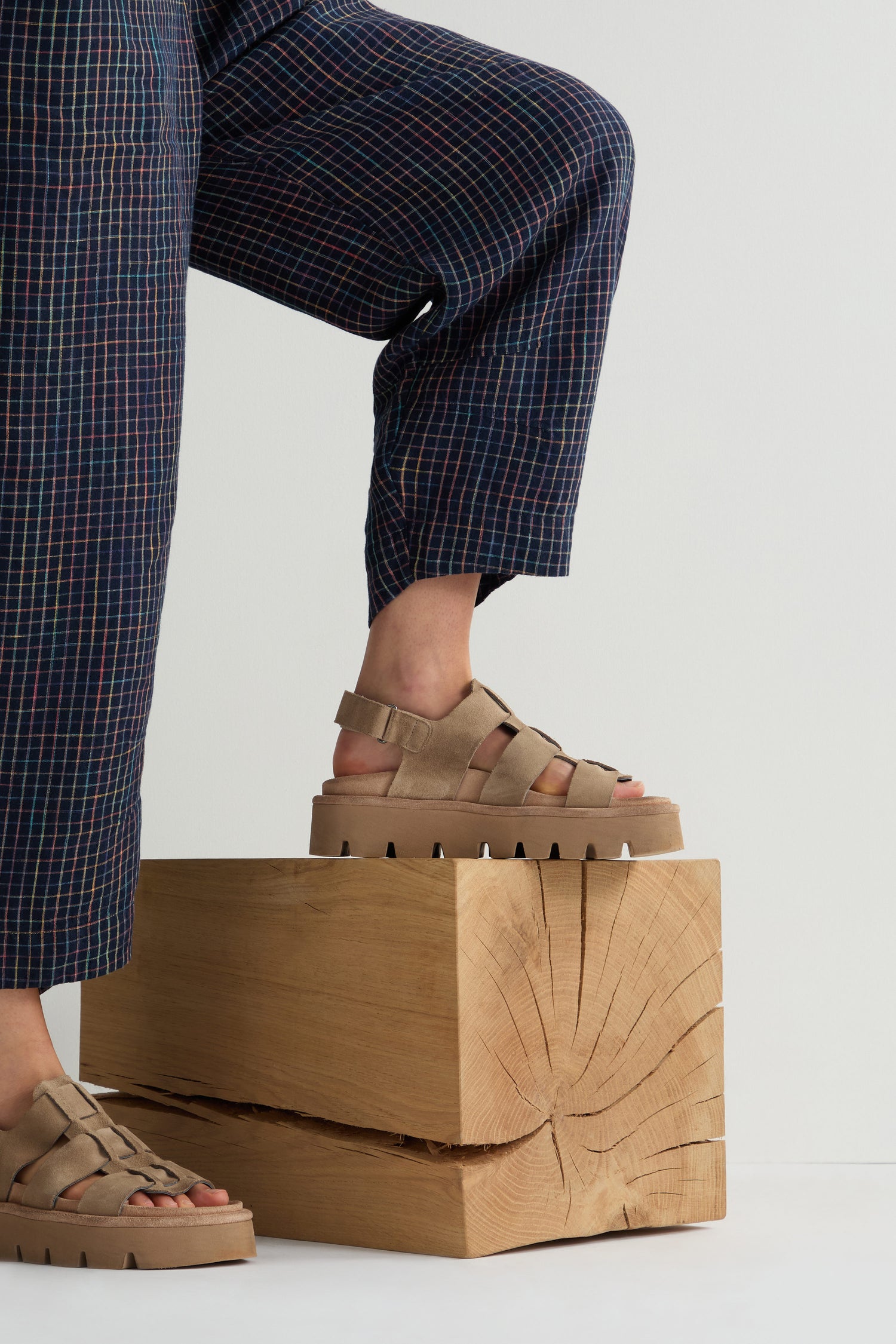 A person in plaid pants and Italian-crafted Suede Platform Velcro Sandals in beige rests one foot on a wooden cube.