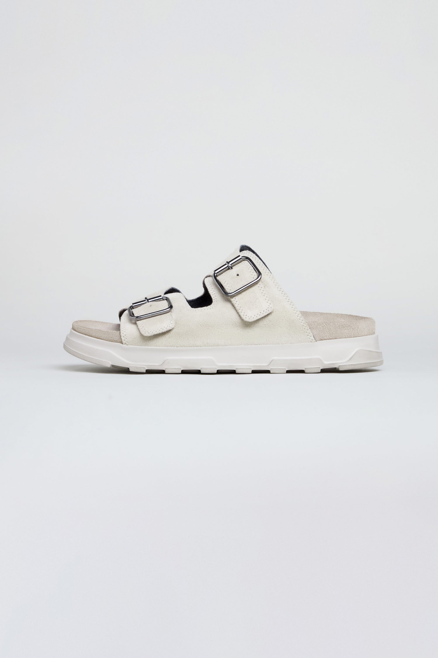 The Double Buckle Suede Sliders, shown in a side view against a plain background, are handcrafted in Italy with two adjustable buckle straps and a cushioned sole.