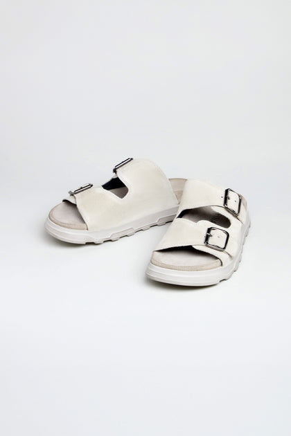 A pair of Double Buckle Suede Sliders handcrafted in Italy, featuring two adjustable buckle straps in suede, displayed on a plain white background.