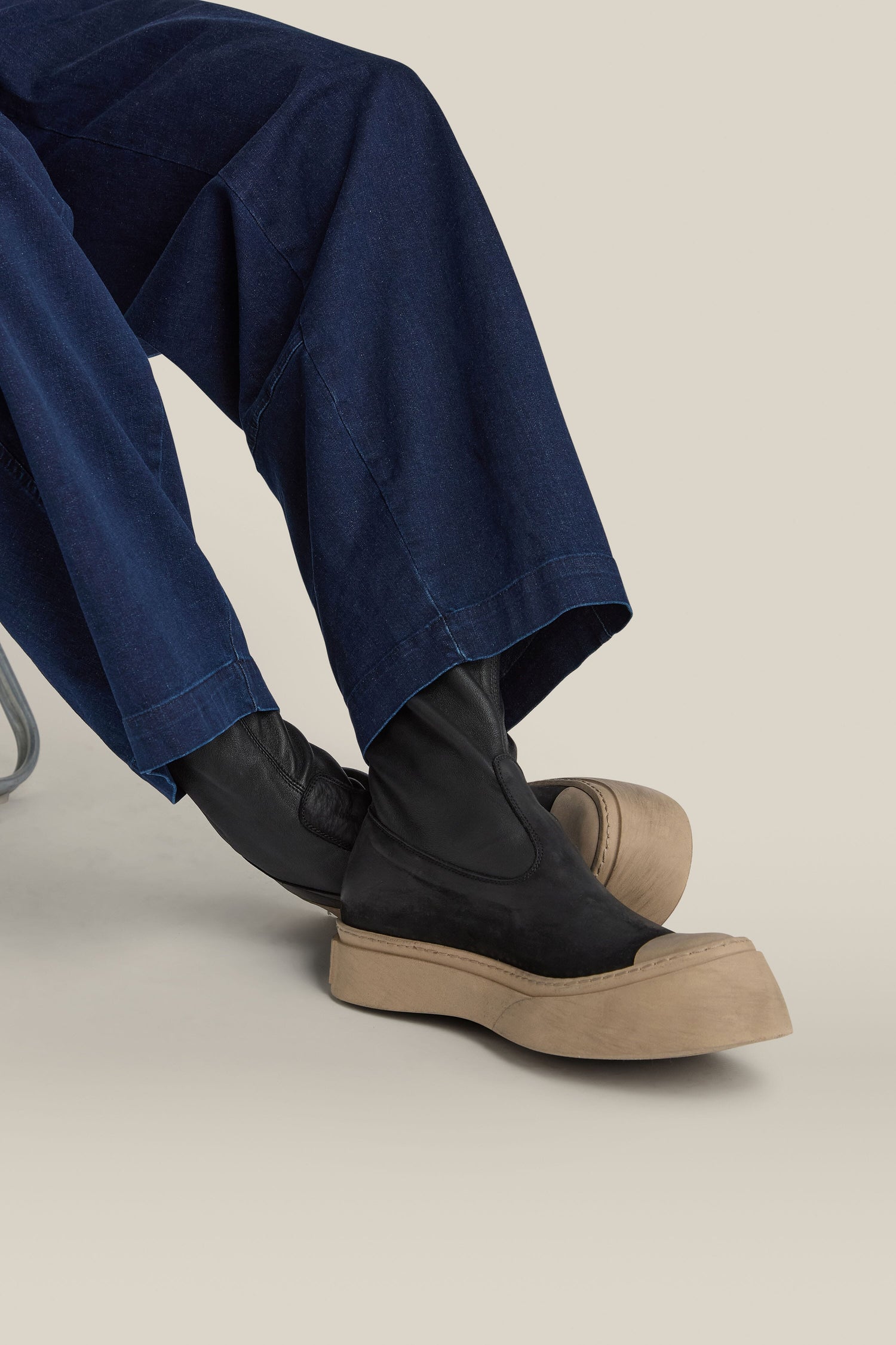 A person seated in blue denim pants and Lofina Contrast Leather Stretch Boots, made from ultra-soft calfskin and featuring thick beige soles, against a plain background.