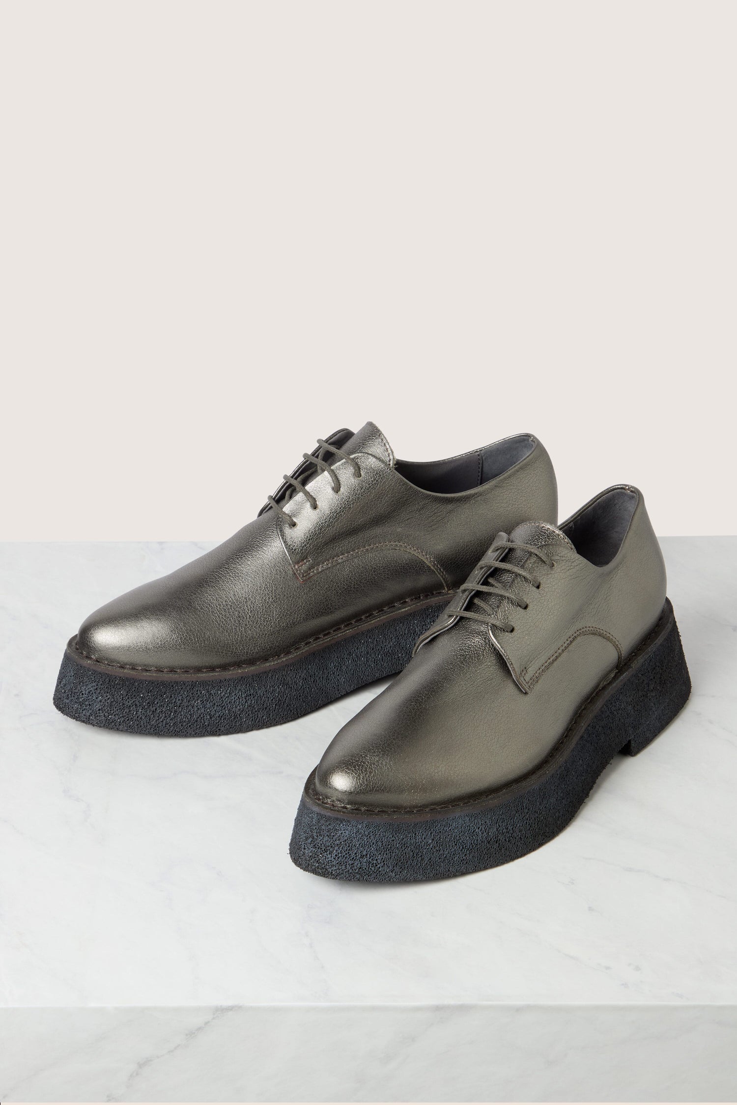 A pair of Lace up Leather Brogues in metallic grey with black, lightweight platform soles displayed on a marble surface.