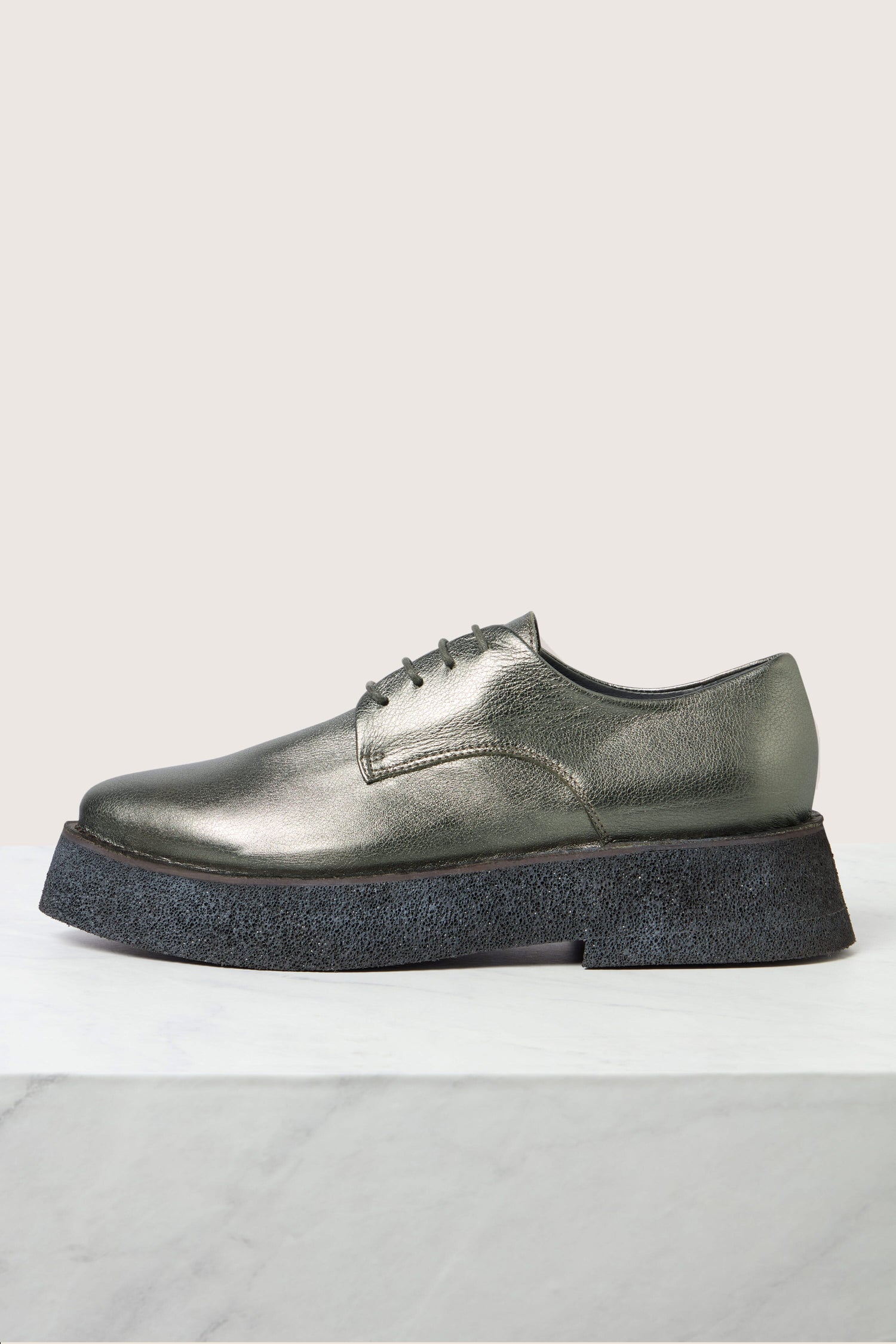 A pair of Lace up Leather Brogues in metallic silver, featuring a thick black textured sole and lightweight platform, is displayed on a light grey marble surface.