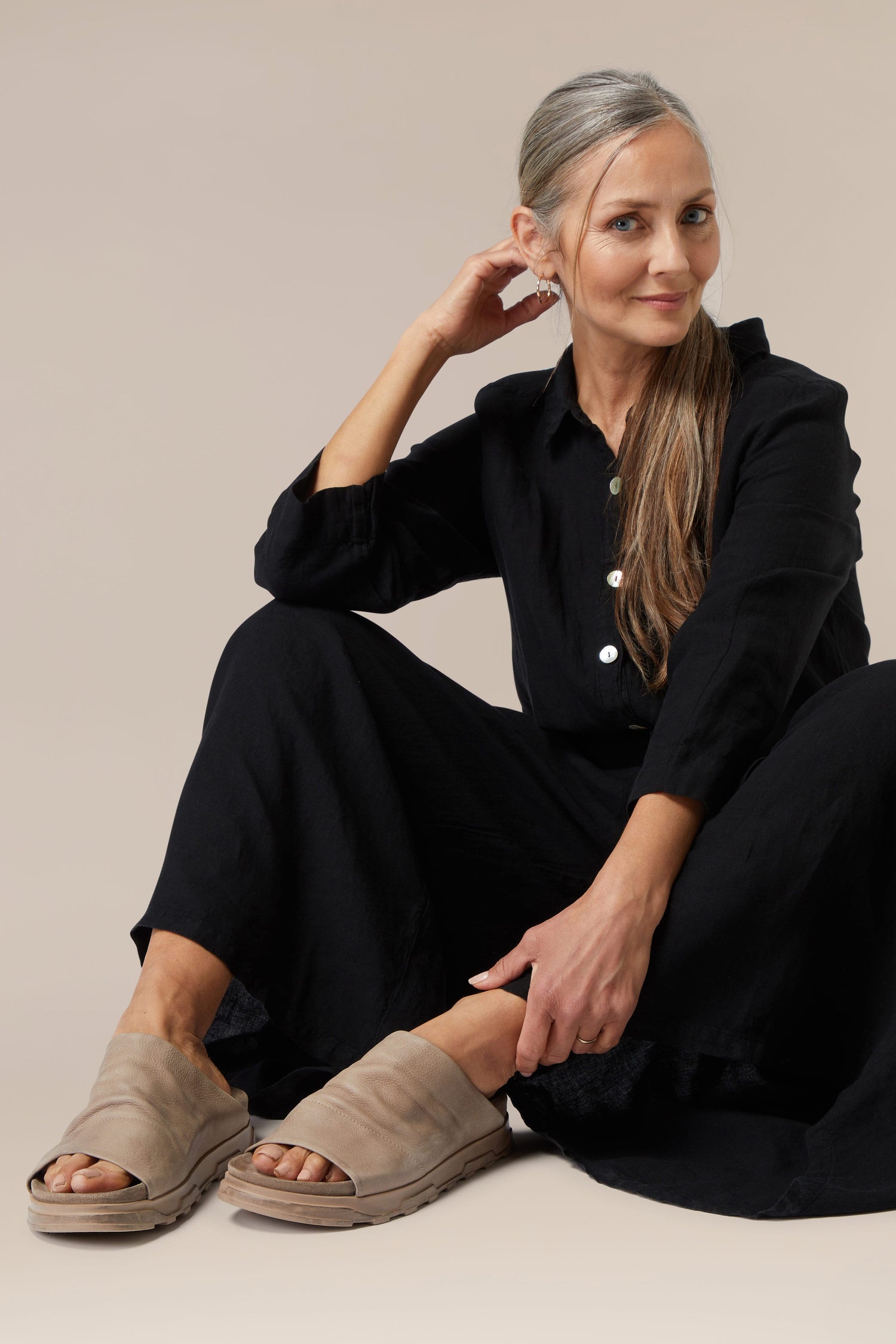 Woman sitting elegantly in a black outfit with Crushed Leather Sliders against a neutral background.