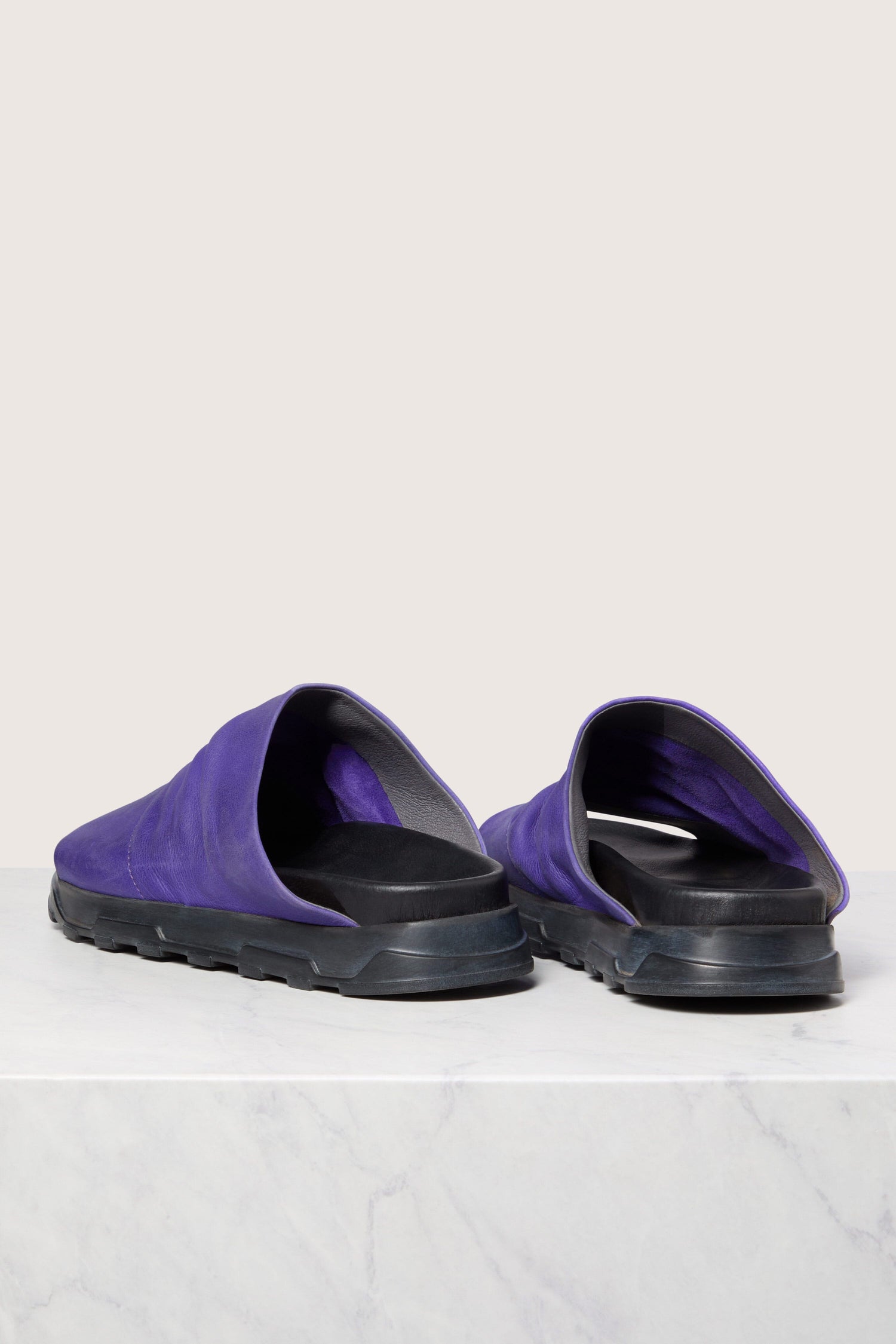 A pair of purple Crushed Leather Sliders on a white marble surface.