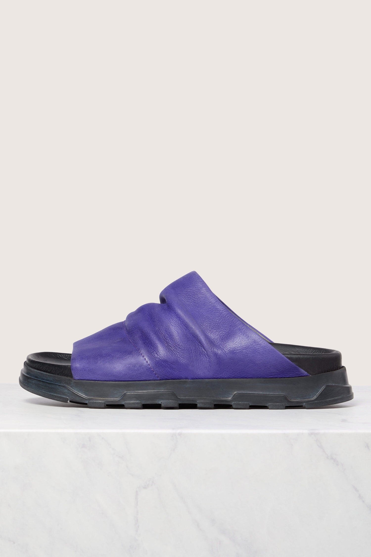 A single purple Crushed Leather Slider sandal with Italian construction on a marble surface against a white background.