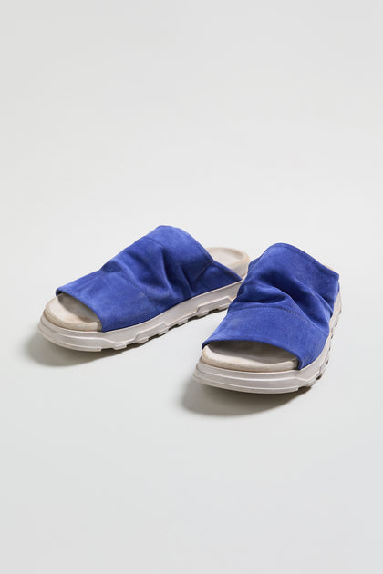 The Crushed Suede Sliders, style LOFI3364, feature blue suede uppers and white textured soles against a light background—an effortless pick for SS26.