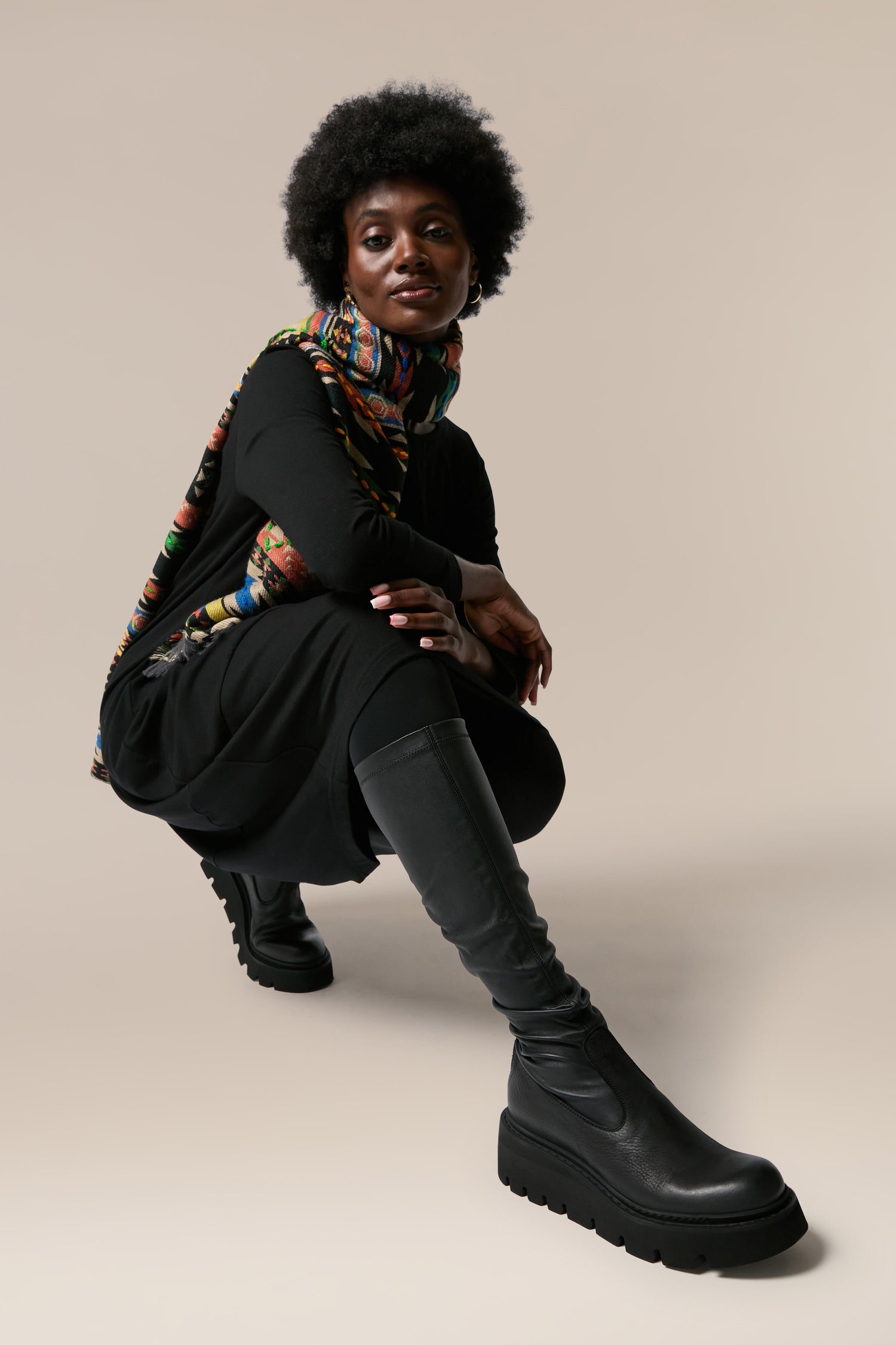 A black woman showcasing a pair of Long Stretch Leather Boots, known for their Italian craftsmanship and Danish design, while crouching in front of a white background.