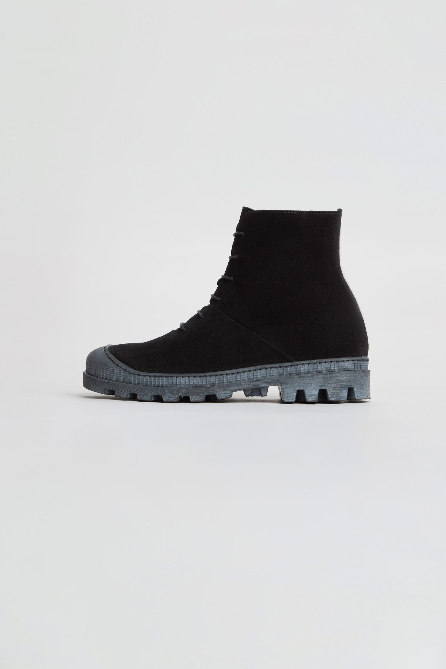A single Lace Up Suede Boot in black, featuring a thick, textured gray sole, is displayed against a plain white background to highlight the modern silhouette of these chunky ankle boots.