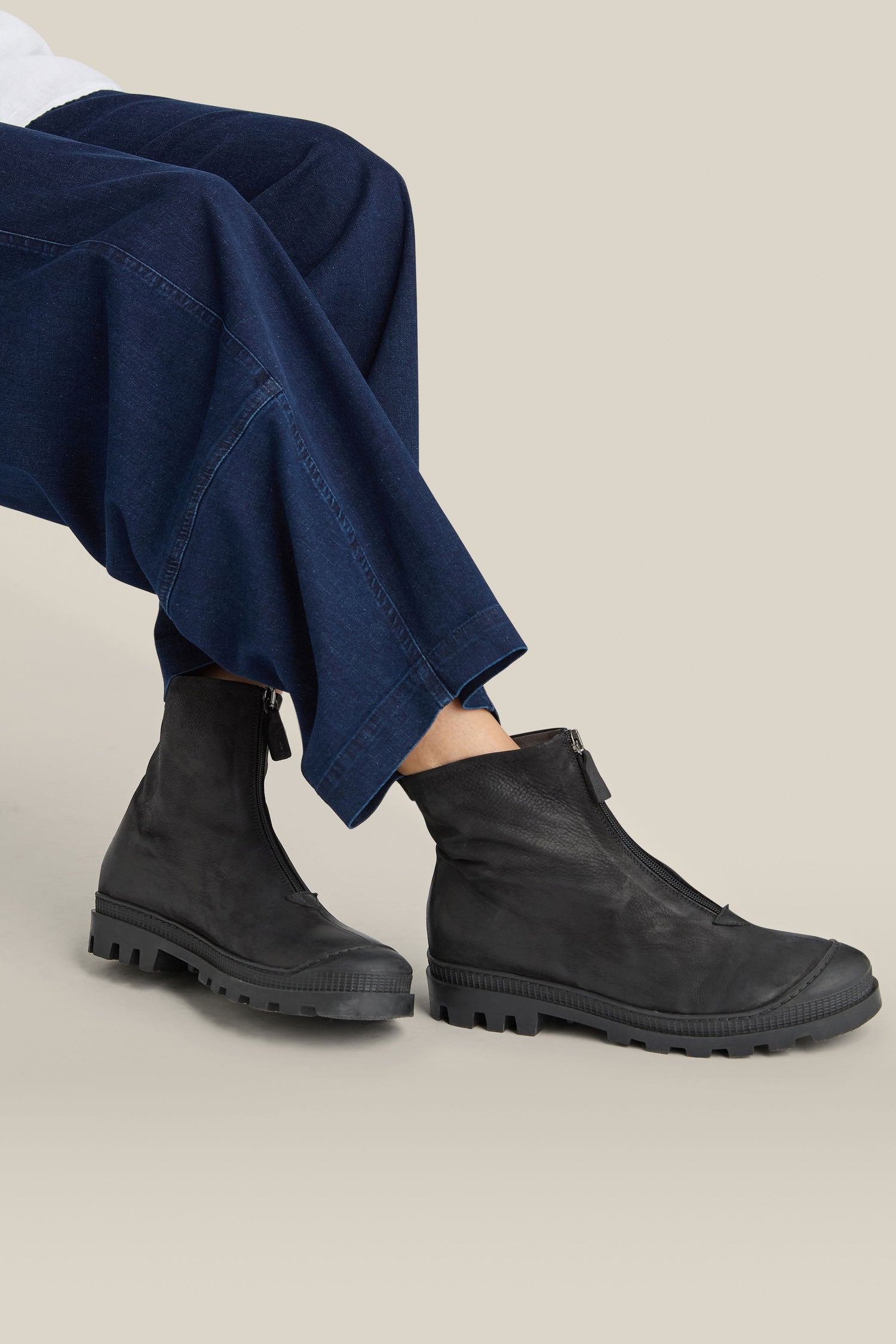 Person wearing dark denim pants and sleek black calfskin "Zip Front Leather Boots" with rugged soles.