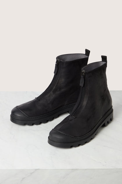 A pair of Zip Front Leather Boots by Lofina, crafted from black calfskin leather with short zip fronts and lug soles, are placed on a white marble surface.