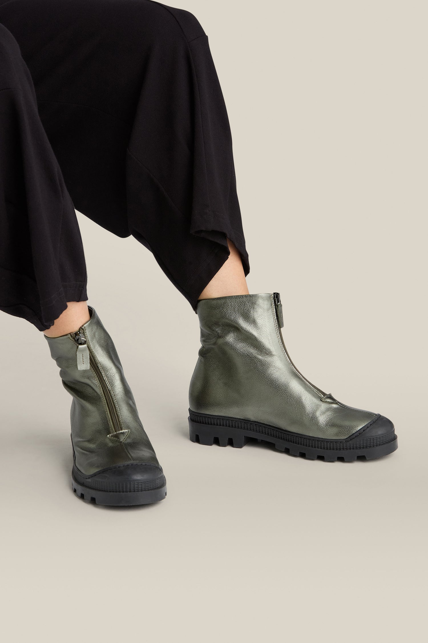 Person wearing Zip Front Leather Boots in metallic green with black soles, paired with black pants, seated against a light beige background.