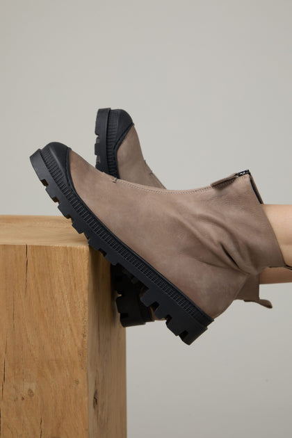 A person wearing Biscotti Zip Front Leather Boots with thick black soles rests their feet on a wooden block against a neutral background.