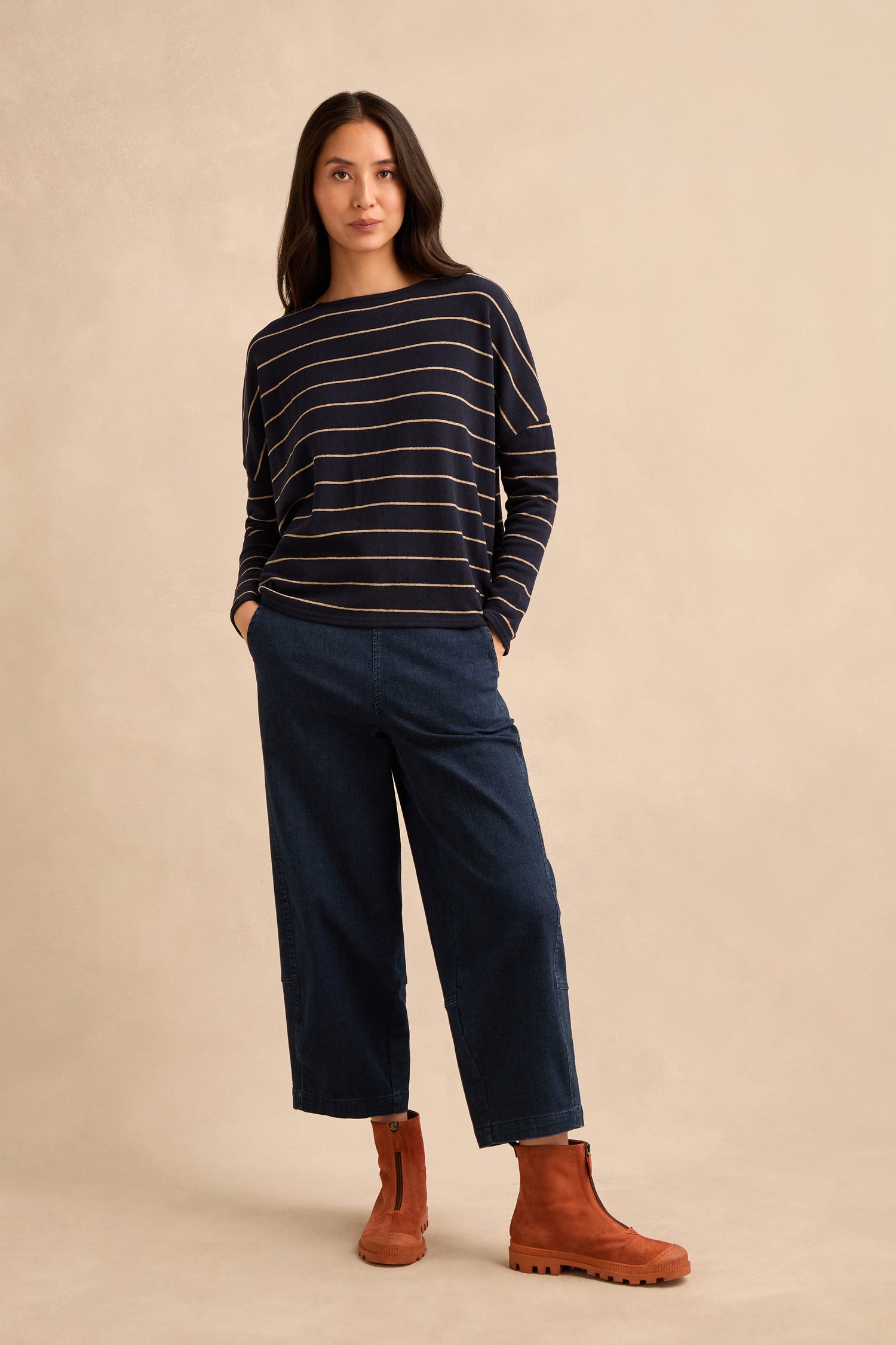 Woman standing against beige background, wearing a navy striped long-sleeve shirt, wide-leg dark jeans, and Zip Front Suede Boots handmade in Italy.