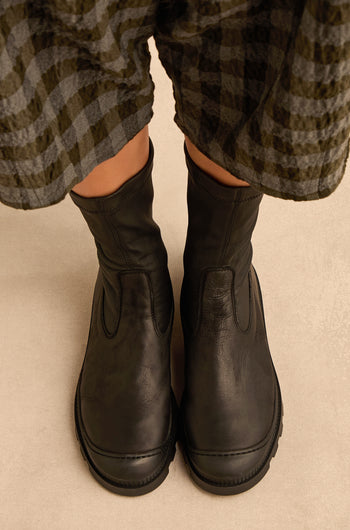 Person wearing Stitch Detail Napa Leather Stretch Boots in black and a plaid skirt, standing on a beige surface.