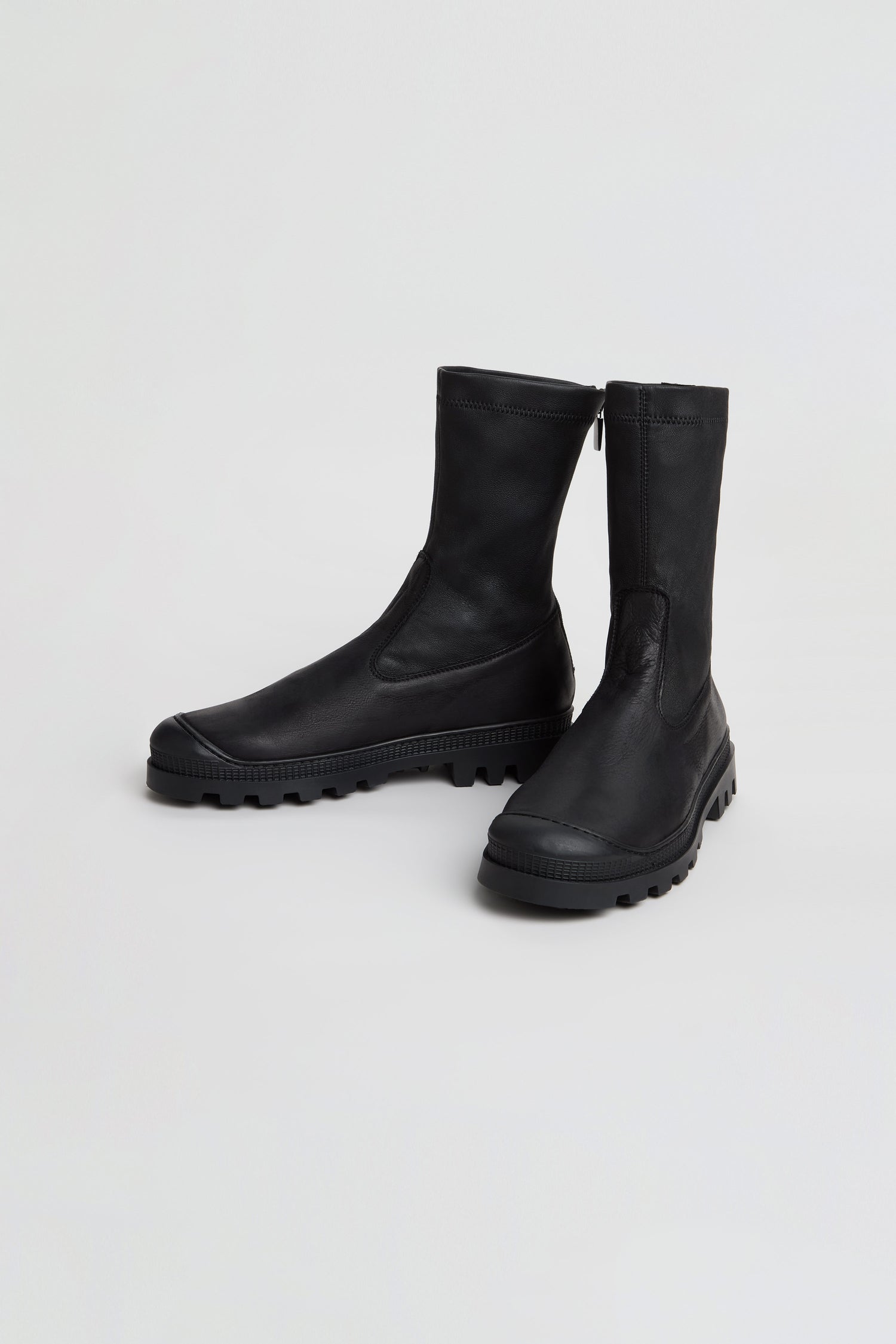 A pair of Stitch Detail Napa Leather Stretch Boots in black, featuring rugged rubber soles and a mid-calf silhouette, are positioned on a plain white background.