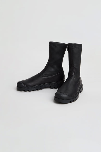 A pair of Stitch Detail Napa Leather Stretch Boots in black, featuring rugged rubber soles and a mid-calf silhouette, are positioned on a plain white background.