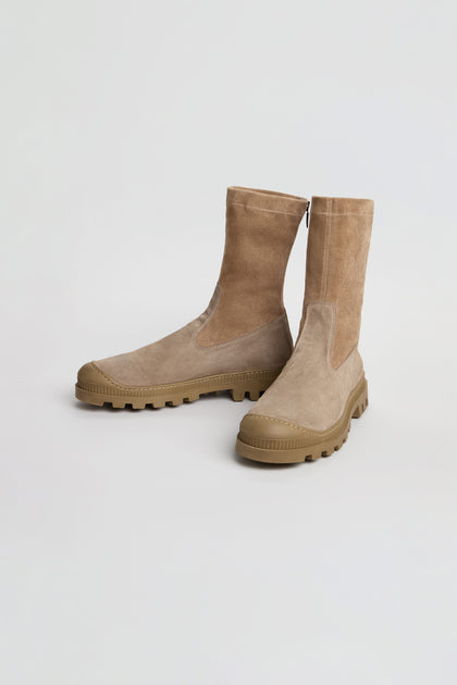 A pair of Stitch Detail Suede Stretch Boots in taupe suede, handmade in Italy with textured rubber soles and a stylish mid-calf silhouette, displayed on a plain white background.