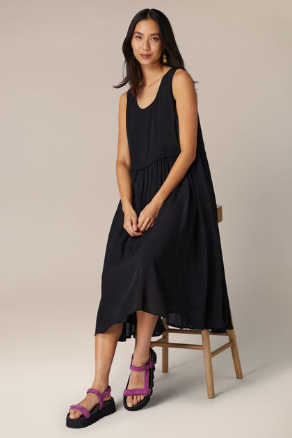 Woman posing in a black sleeveless midi dress and Scandinavian-designed purple suede Velcro sandals.