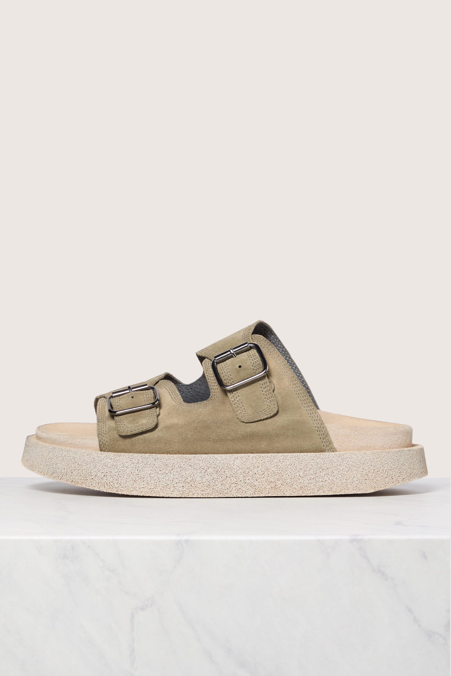 Olive "Suede Double Buckle Slider" with two adjustable straps on a cork footbed against a marble background, embodying Italian construction.