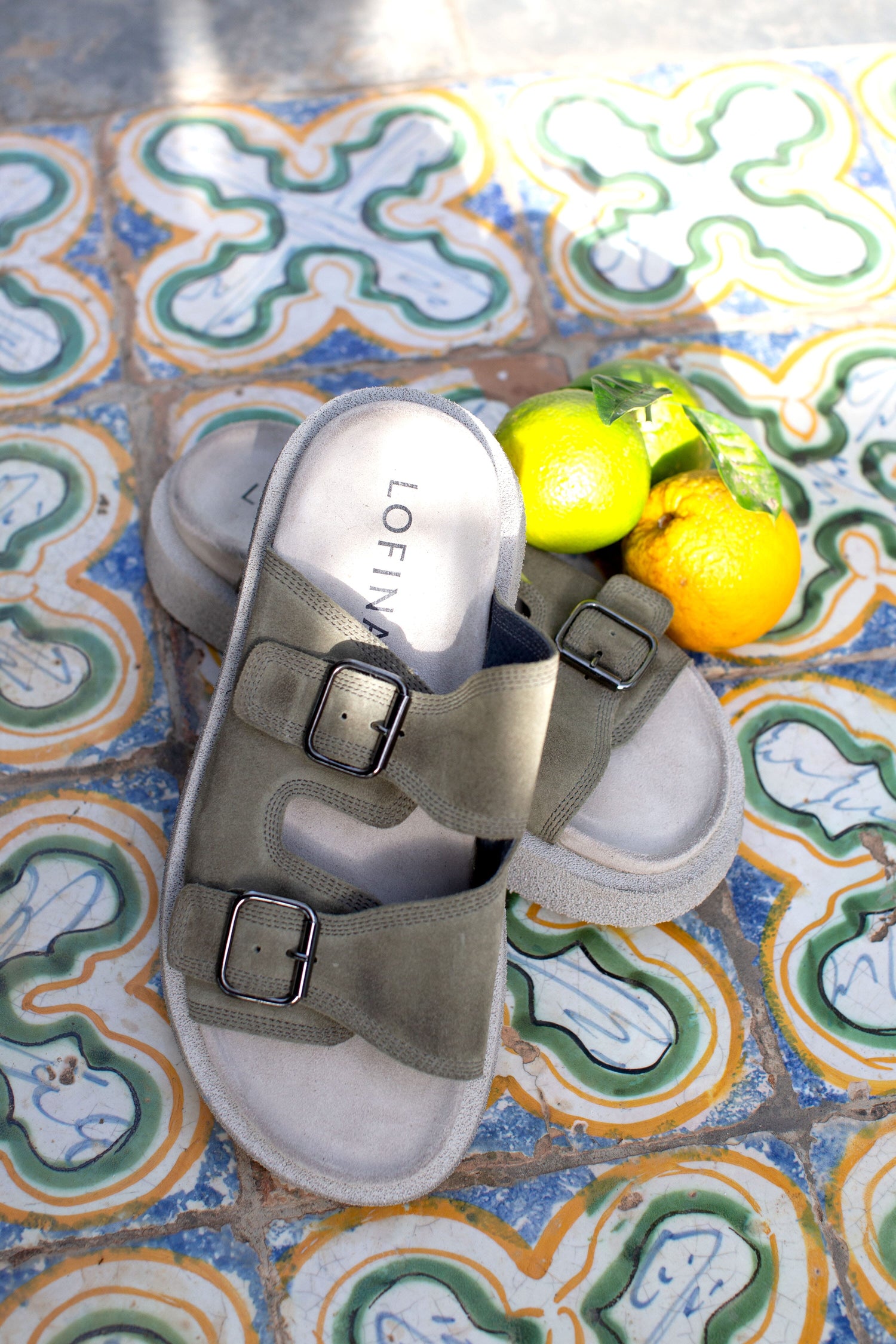 A pair of Suede Double Buckle Buckle Slider on a tile floor.